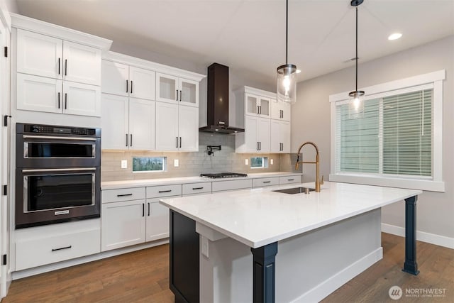 kitchen featuring tasteful backsplash, gas stovetop, a sink, double wall oven, and wall chimney exhaust hood