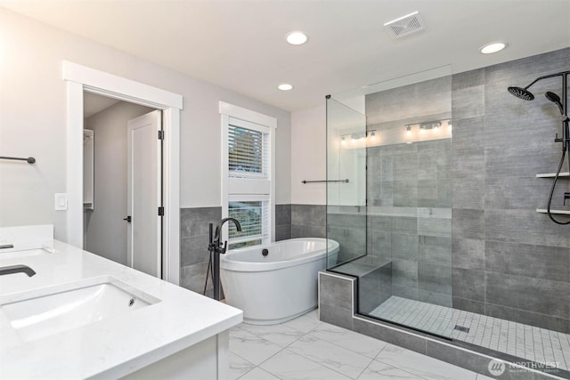 bathroom with double vanity, a sink, a tile shower, and tile walls