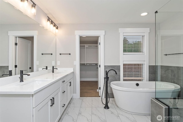 full bath featuring double vanity, a sink, marble finish floor, and a freestanding tub