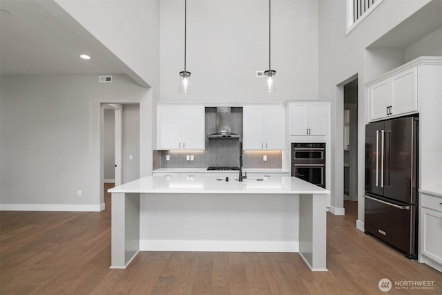 kitchen featuring dobule oven black, a high ceiling, wall chimney range hood, and high quality fridge