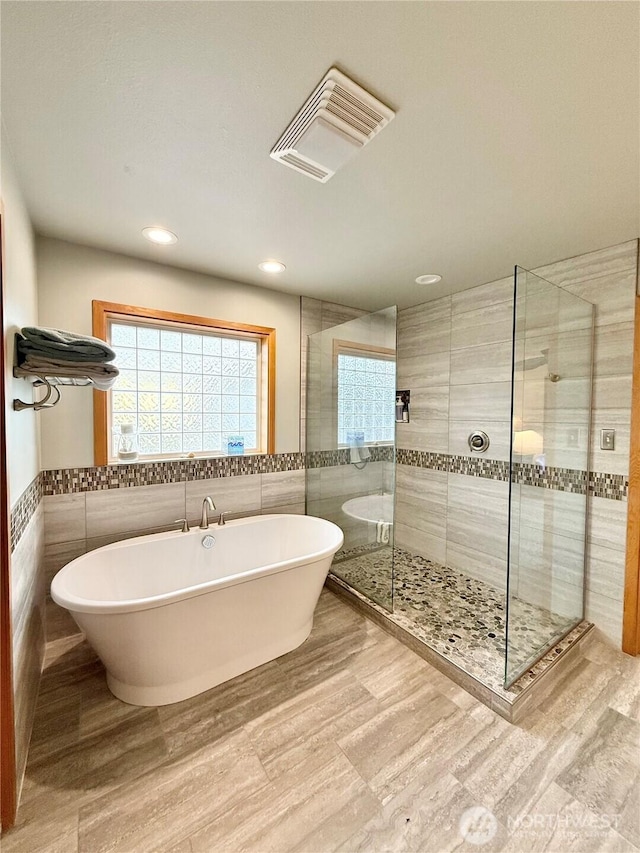 bathroom featuring tile walls, visible vents, a soaking tub, and a shower stall