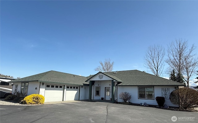 ranch-style home featuring a shingled roof, an attached garage, and aphalt driveway