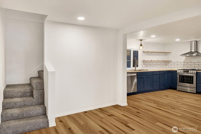 13574 S Green St, Anacortes, WA 98221 - kitchen with wall chimney range hood, stainless steel appliances, backsplash, light wood-style flooring, and blue cabinetry