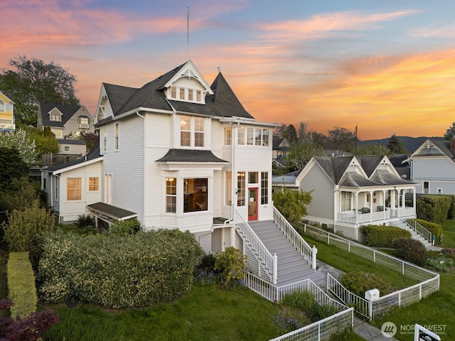 back of property at dusk featuring roof with shingles and fence