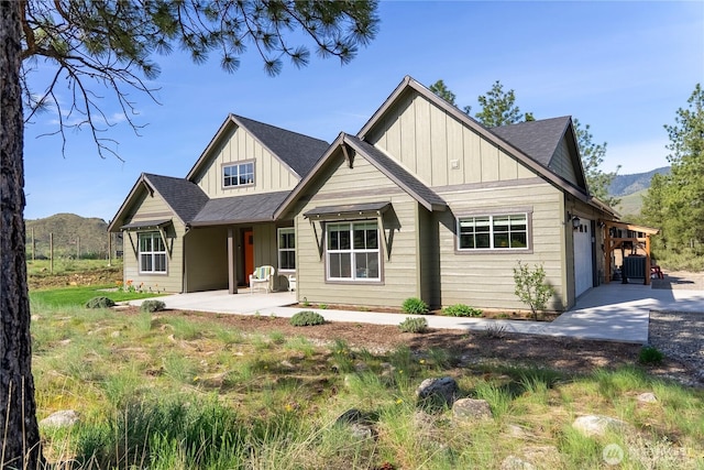 view of front of home with roof with shingles, board and batten siding, a patio area, an attached garage, and a mountain view
