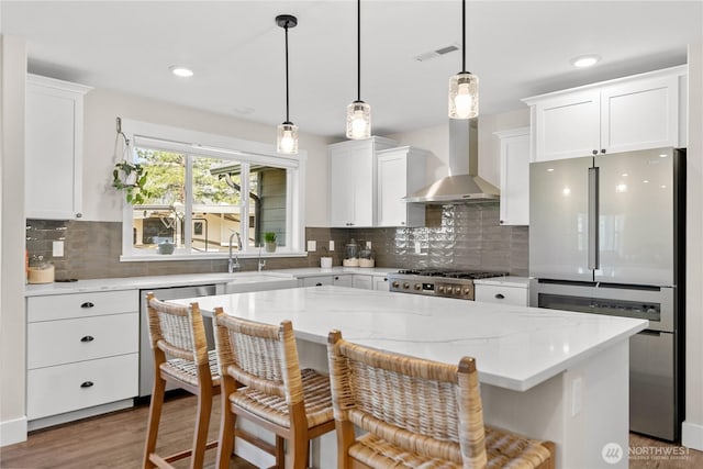 kitchen with visible vents, appliances with stainless steel finishes, wall chimney exhaust hood, a sink, and white cabinetry