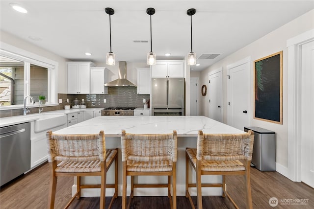 kitchen with wall chimney range hood, white cabinets, a sink, stainless steel appliances, and dark wood-type flooring