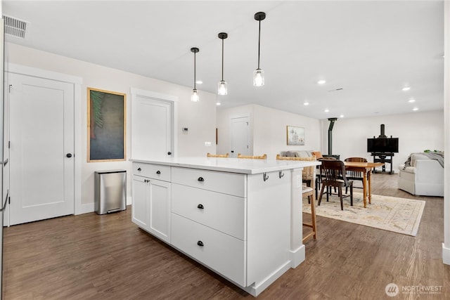 kitchen with visible vents, a wood stove, a kitchen island, open floor plan, and dark wood finished floors