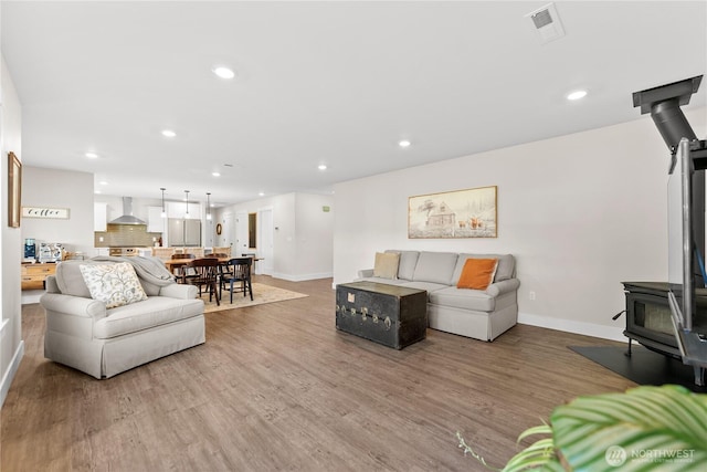 living room featuring baseboards, a wood stove, wood finished floors, and recessed lighting