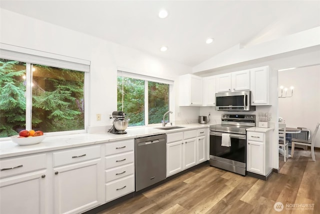 kitchen featuring white cabinets, wood finished floors, stainless steel appliances, lofted ceiling, and a sink