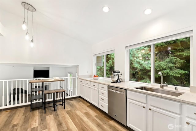 kitchen featuring white cabinetry, light wood-type flooring, stainless steel dishwasher, a sink, and light stone counters