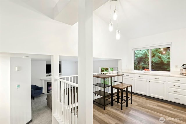 interior space with high vaulted ceiling, light countertops, a warm lit fireplace, white cabinets, and light wood-style floors