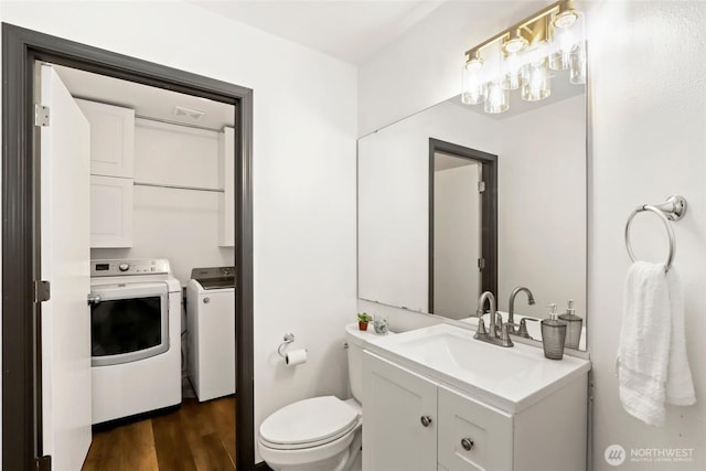 bathroom featuring washing machine and clothes dryer, visible vents, wood finished floors, toilet, and vanity
