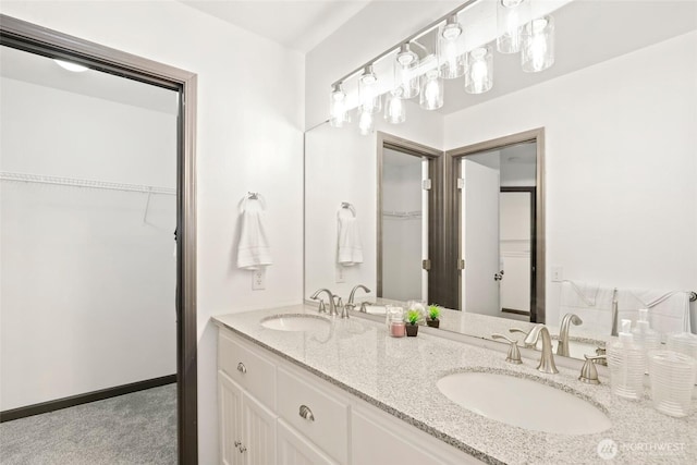full bath with baseboards, double vanity, a sink, and a walk in closet
