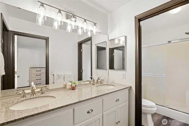 bathroom featuring double vanity, a sink, toilet, and a shower stall