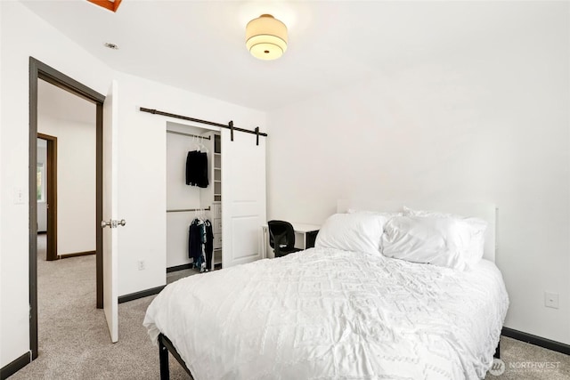 carpeted bedroom featuring a closet, a barn door, and baseboards