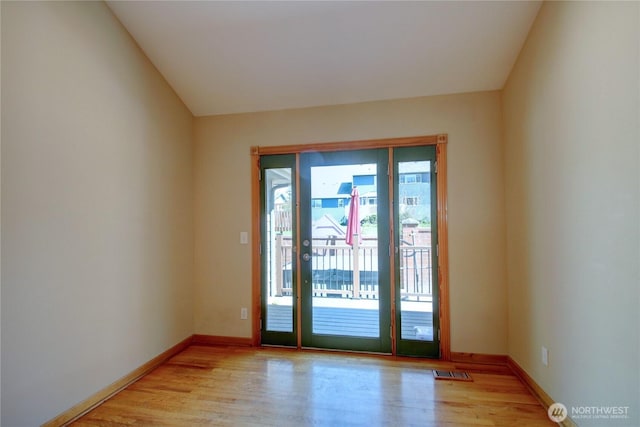 doorway with light wood finished floors, baseboards, vaulted ceiling, and visible vents