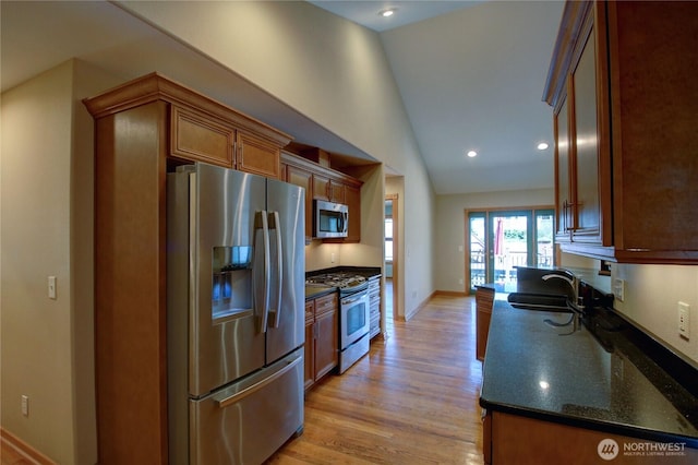 kitchen featuring light wood finished floors, a sink, baseboards, lofted ceiling, and appliances with stainless steel finishes