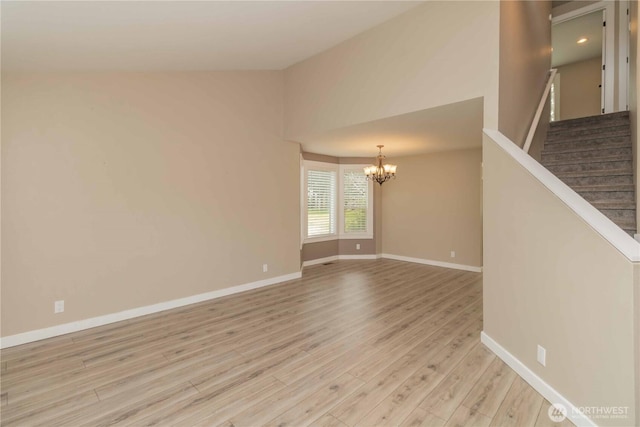 spare room featuring light wood-style flooring, baseboards, stairway, lofted ceiling, and a notable chandelier