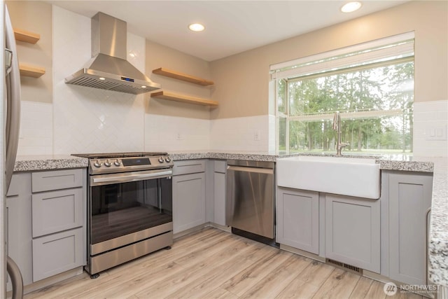 kitchen with wall chimney range hood, appliances with stainless steel finishes, gray cabinetry, and open shelves