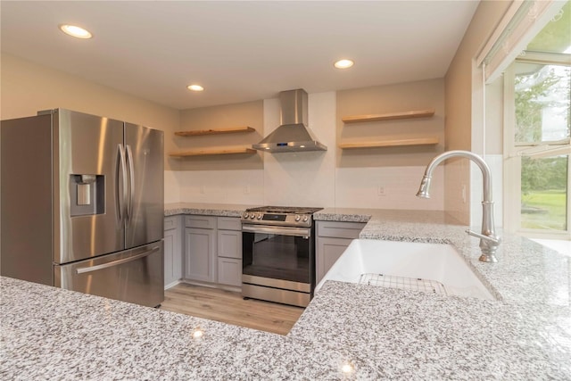 kitchen featuring a sink, open shelves, light stone countertops, appliances with stainless steel finishes, and wall chimney range hood