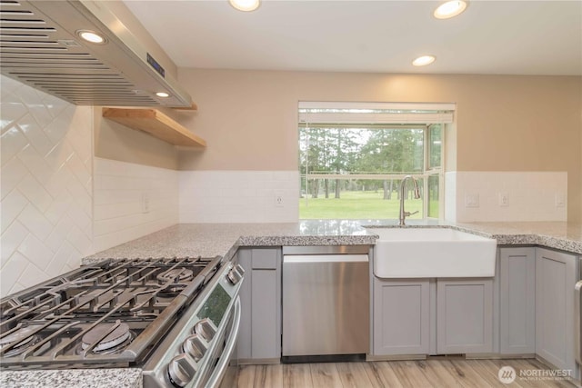 kitchen featuring gray cabinetry, exhaust hood, light stone counters, and appliances with stainless steel finishes