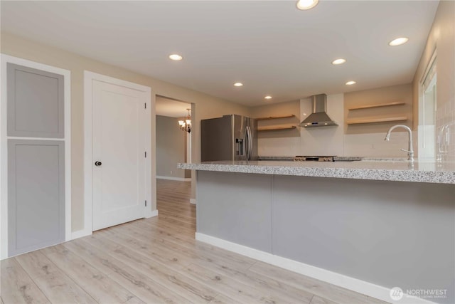 kitchen with stainless steel refrigerator with ice dispenser, open shelves, a sink, light wood-style flooring, and wall chimney exhaust hood