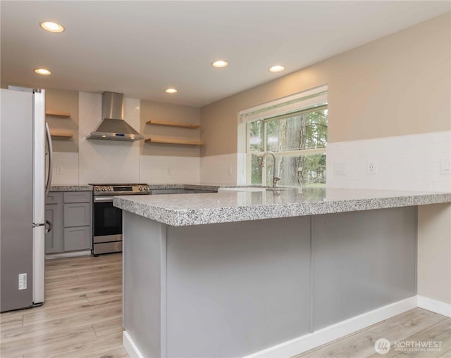 kitchen with a peninsula, stainless steel appliances, open shelves, wall chimney range hood, and gray cabinets