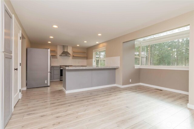 kitchen with recessed lighting, range, light wood finished floors, freestanding refrigerator, and wall chimney exhaust hood