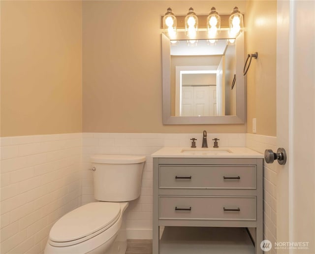 bathroom featuring toilet, vanity, tile walls, and wainscoting