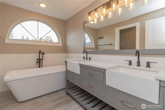 full bath with double vanity, a sink, a freestanding tub, and wood finished floors