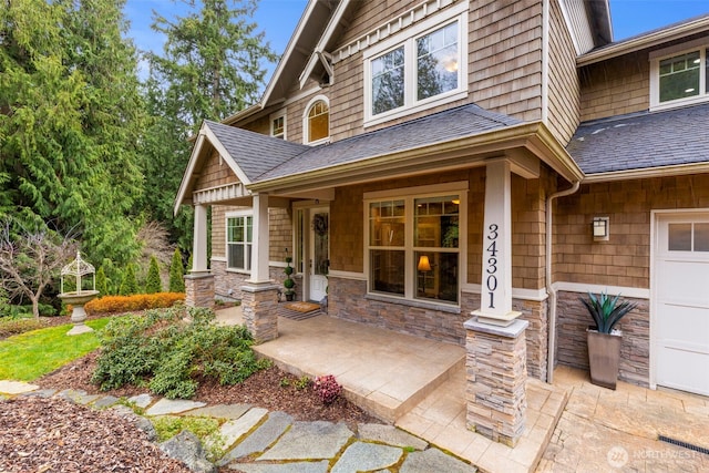doorway to property with a shingled roof, a porch, and stone siding