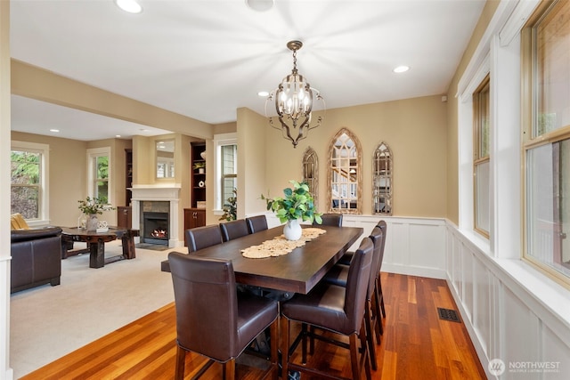 dining space with a fireplace with flush hearth, wainscoting, a decorative wall, visible vents, and an inviting chandelier