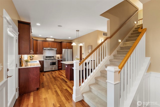 kitchen featuring light countertops, wood finished floors, stainless steel appliances, under cabinet range hood, and a sink