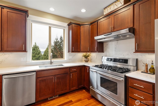 kitchen with light countertops, stainless steel appliances, under cabinet range hood, a sink, and visible vents