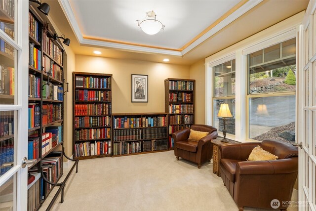 living area with carpet flooring, a raised ceiling, crown molding, and wall of books