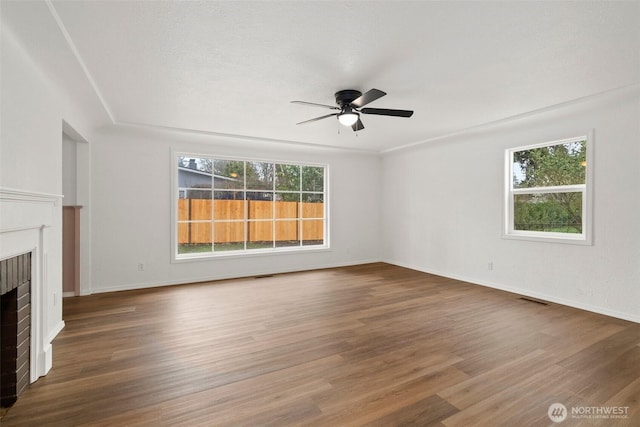unfurnished living room with wood finished floors, a ceiling fan, visible vents, baseboards, and a brick fireplace