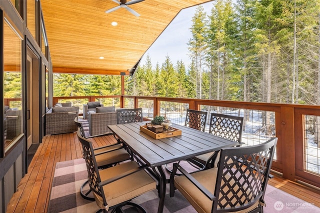 deck featuring a view of trees, an outdoor living space, a ceiling fan, and outdoor dining space