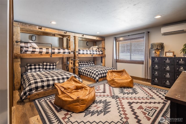 bedroom featuring baseboards, a wall unit AC, recessed lighting, and wood finished floors