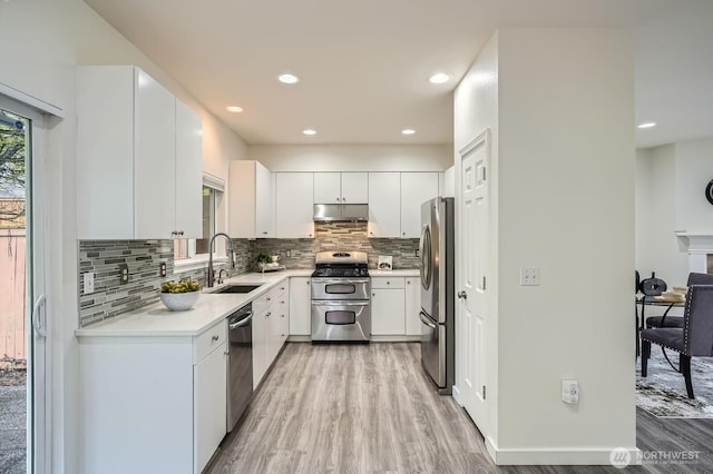 kitchen with a sink, light wood-style floors, light countertops, stainless steel appliances, and tasteful backsplash