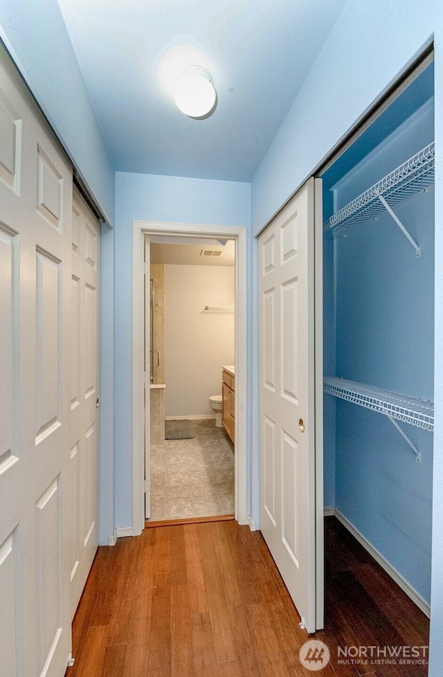 hall featuring visible vents, baseboards, and wood finished floors