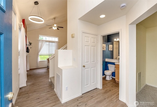 hallway featuring visible vents, light wood finished floors, baseboards, and vaulted ceiling