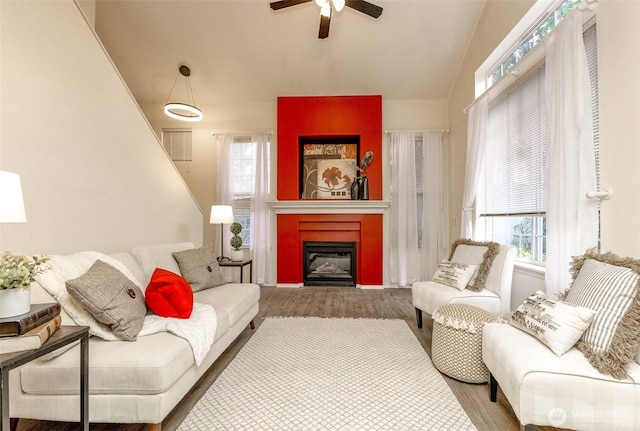 living area featuring ceiling fan, a glass covered fireplace, vaulted ceiling, and a wealth of natural light