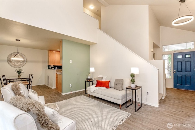 living area with high vaulted ceiling, stairs, light wood-style floors, and baseboards