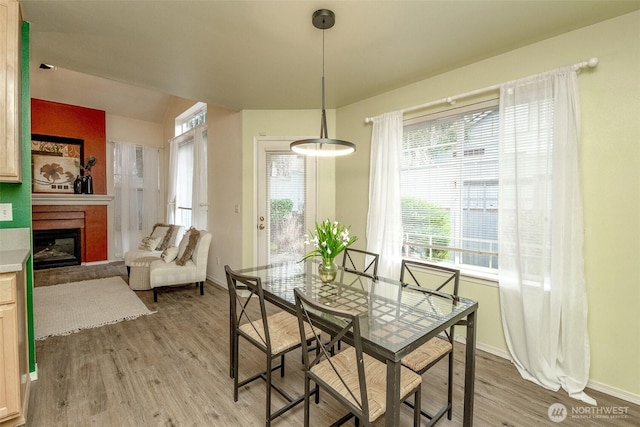 dining room featuring a fireplace, light wood finished floors, and baseboards