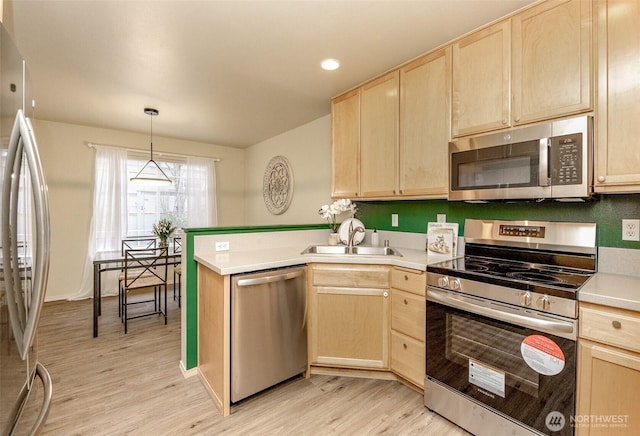 kitchen featuring a sink, a peninsula, light brown cabinetry, and stainless steel appliances