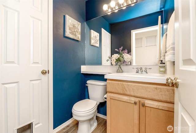 half bathroom featuring vanity, baseboards, toilet, and wood finished floors