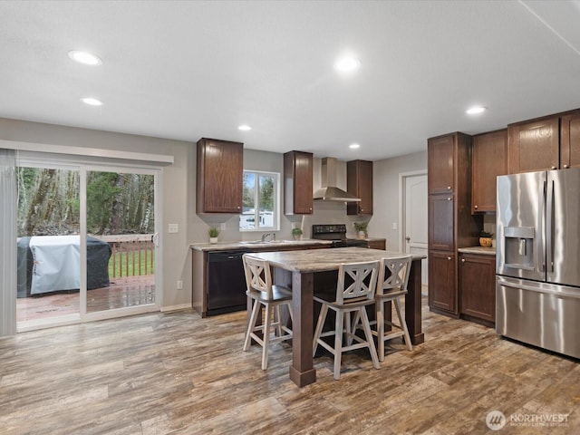 kitchen featuring wall chimney range hood, a kitchen breakfast bar, black appliances, and light wood-type flooring