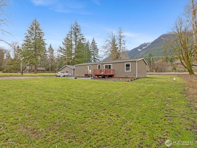 rear view of property with a deck with mountain view and a lawn