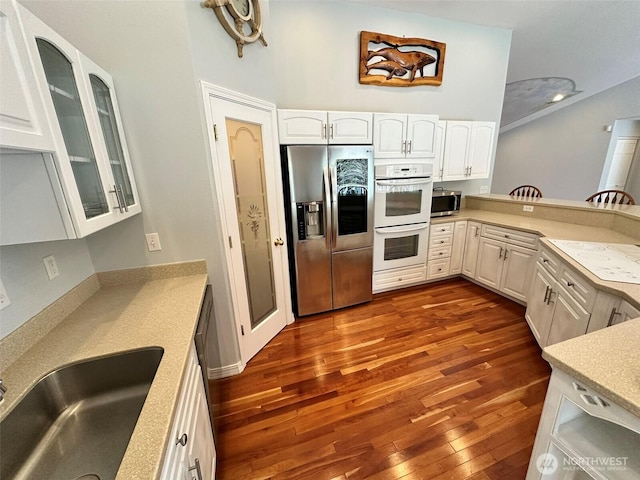 kitchen with white cabinetry, light countertops, dark wood finished floors, appliances with stainless steel finishes, and glass insert cabinets